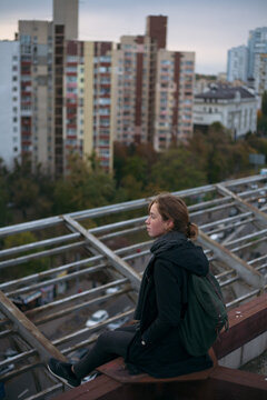girl sitting on the edge of the roof against the background of high-rise buildings