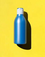 Blue plastic bottle on yellow background with hard shadow. Bottle with cosmetic cream for hair. Template clean bottle. Flat lay, top view.