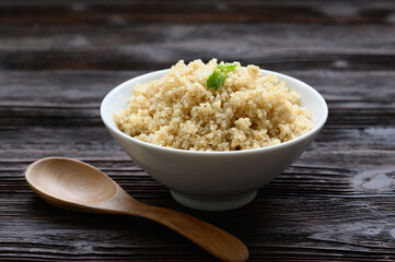 Bowl of boiled quinoa on wood background