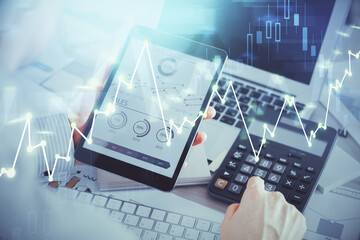 Double exposure of man's hands holding and using a digital device and forex graph drawing. Financial market concept.