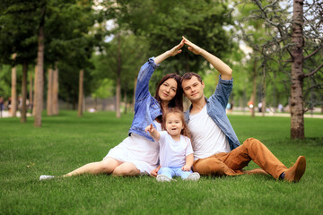 Fototapeta premium Cheerful happy family embracing and looking at camera while resting on green grass on sunny day in park