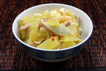 Traditional spicy side dish menu in Asia restaurant. Cutting pickled lettuce with chilly, sliced fresh shallot and boiled chicken egg in the bowl. Famous appetizer menu on the wooden mat. 