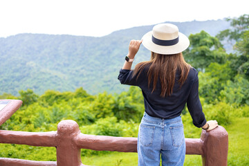 Fototapeta premium Woman wearing a hat, black shirt, blue jeans standing looking mountian view.