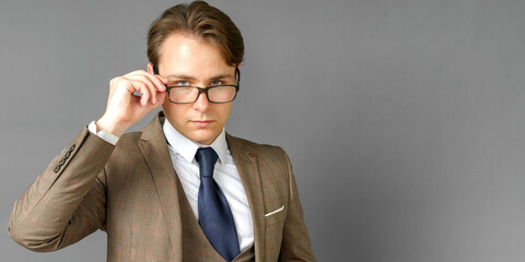 Portrait of a businessman in a suit looking at the camera and adjusting his glasses. Gray background.