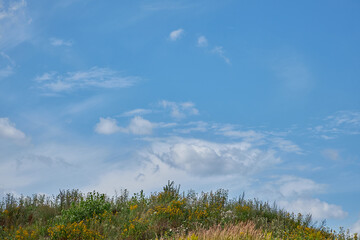 A grassy hill against a blue sky with clouds