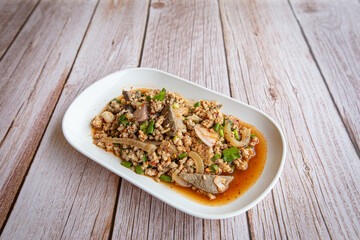 Thai food, spicy minced pork salad (Larb Moo) in white plate on wooden table, popular local food in northeastern Thailand