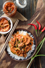 Stir- fried kimchi with pork on cooked rice in a bowl on wooden background, Korean food