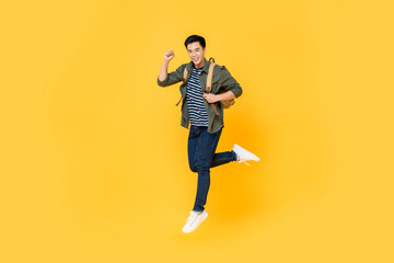 Fototapeta na wymiar Happy smiling young Asian tourist man with backpack jumping in mid-air isolated on yellow background