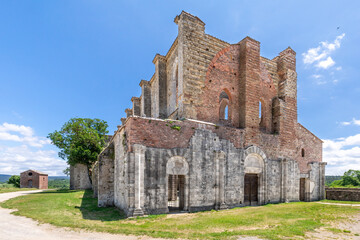 Wide angle view of the ruins of an ancient gothic cathedral with a tree growing on its side, against a blue summer sky with sparse clouds