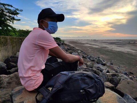 Men in medical mask setting alone on beach, safe travel in Covid19  - Powered by Adobe