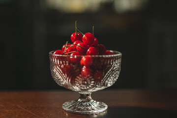a bowl full of red cherries. there are many cherries and they look very sweet and juicy. they are freshly harvested from the garden and the bowl is on a wooden table. fruits and veggies are yummy