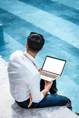 Freelance businessman. Young handsome man with laptop while sitting near swimming pool.