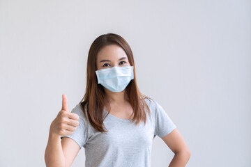 Portrait of cheerful young Asian girl with protective face mask thumb up posing and smiling at camera over white background. Copy space