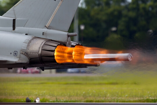 Afterburners glowing on an air force fighter jet aircraft as it speeds down the runway of an air base.