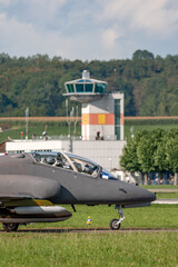 Air Force jet trainer aircraft taxiing at an airbase with the air traffic control tower behind.