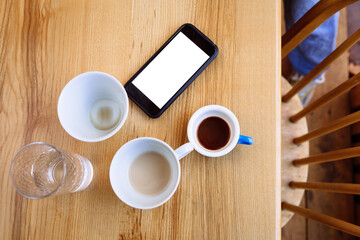 Dirty coffee cups, cappuccino and a glass of water stand on a wooden table. Next to the cups is a telephone. Coffee break. Flat lay