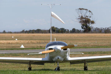 Single engine aircraft at a country airfield with a windsock in the background.