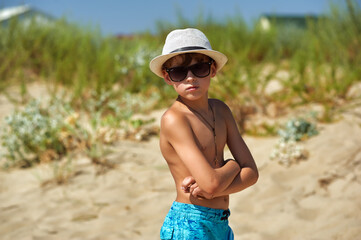tanned boy at the resort . A child in a hat and sunglasses on vacation