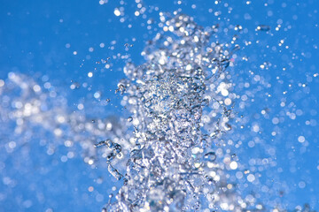 Water droplets spraying from a fountain in abstract design on blue sky background and detail and contrast. Concept.