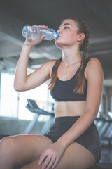 Beautiful young woman drinks water in gym. Sports nutrition concept