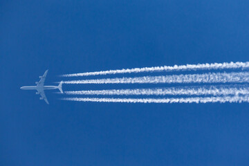 Large four engined commercial airliner jet aircraft flying at high altitude with a large contrail flowing behind it.