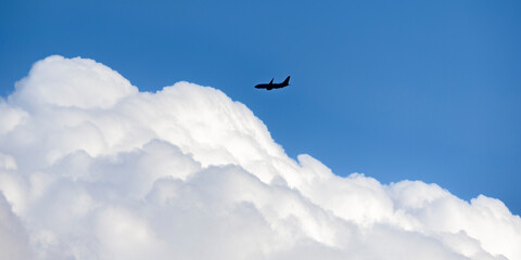 Commercial airliner aircraft flying at high altitude towards large white fluffy clouds.