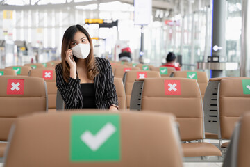 Asian Business woman wearing face mask talking on the phone while sitting on the chair that marked with Social distancing sticker, New normal concept of society with social distancing for public place