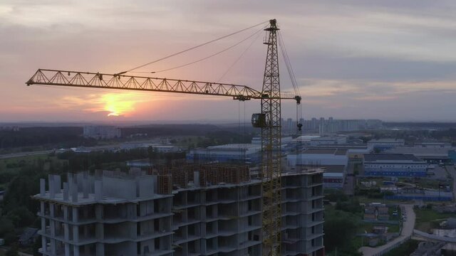 High-rise crane at construction site of house during sunset.