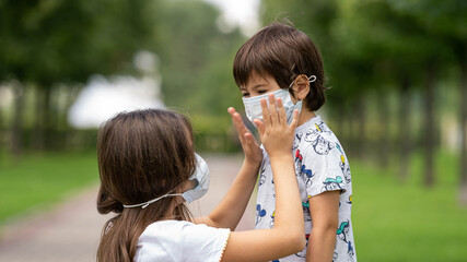 Obraz premium a young girl helps her brother to wear a face mask from the coronavirus covid19