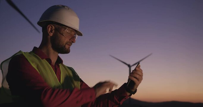 Engineer browses information in the phone standing on the background of windmills at sunset