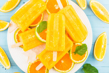 Homemade frosty popsicles with oranges on a blue wooden background