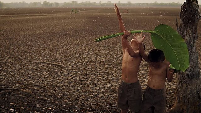 Climate change, Asian boys enjoy with first falling rain season on dry cracked land. Environment conservation and stop global warming concept