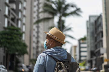Rear view young asian backpacker traveling in urban city wearing face mask for protect virus safety travel.