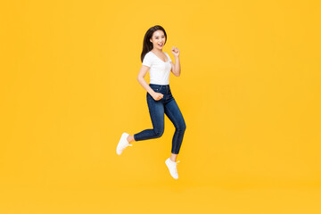 Fototapeta na wymiar Full length portrait of pretty Asian woman smiling and jumping in mid-air isolated on yellow background
