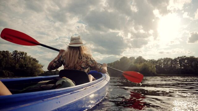 Pretty Woman In Hat Kayaking On Lake At Sunset And Holds Oar.Girl Traveler Swim In Kayak Boat In Tranquil Pond.Girl In Kayak Summer Trip.Woman Exploring Calm River By Canoe On Holiday Vacation Weekend