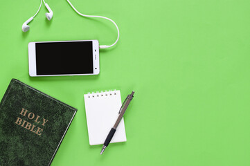 Top view of Holy Bible, phone, and mini notebook on green background