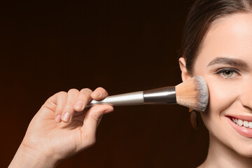 Obraz premium Young woman with makeup brush on dark background