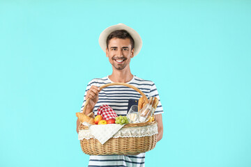 Young man with food for picnic in basket on color background