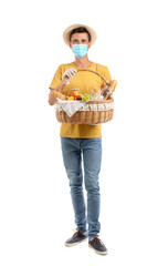 Young man with protective mask and food for picnic in basket on white background