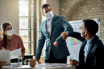 Business colleagues with face masks elbow bumping on a meeting.