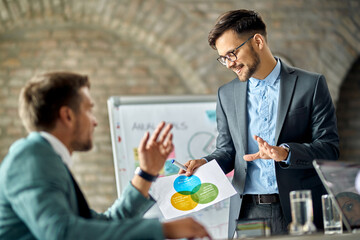 Happy entrepreneurs analyzing data on business charts during a meeting in the office.