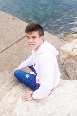 Fototapeta na wymiar Young teenager male sitting on breakwaters while looking at camera
