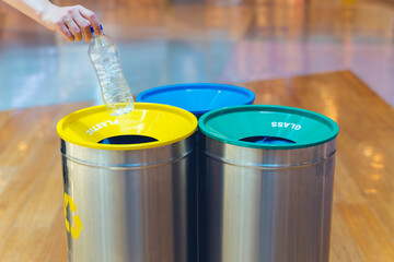 Woman putting empty plastic bottle in recycling bin in the mall. Different trash can with colorful garbage bags.