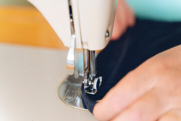 Seamstress sews clothes made of black cloth on a sewing machine. Work by the light of the built-in hardware lamp. Steel needle with looper and presser foot close-up.