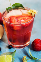 Red cocktail in glass with strawberry, apple and lime