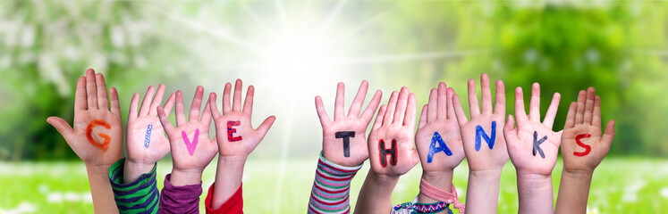 Children Hands Building Colorful English Word Give Thanks. Sunny Green Grass Meadow As Background