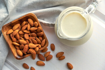 Almond milk in glass with almonds in wooden bowl on a white wooden table