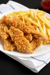 Homemade Crispy Chicken Tenders and French Fries on a white plate on a black background, low angle view. Close-up.