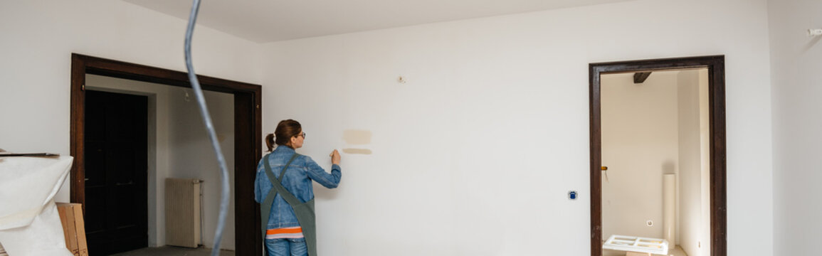Side view of female architect woman testing light paint on the renovated room wall during the general reconstruction of her dream house
