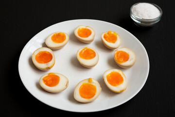 Homemade Unami Soy Sauce Eggs on a white plate on a black background, side view.